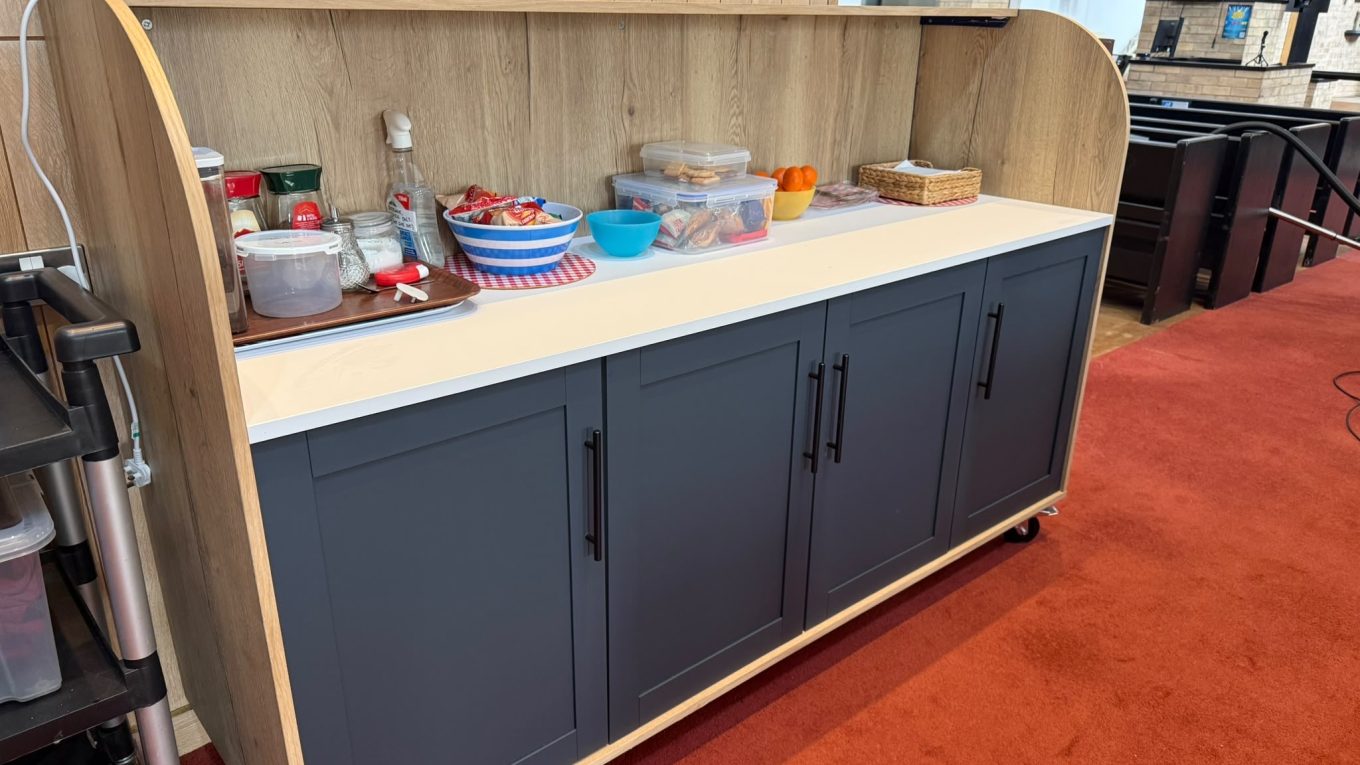The new St Nick's refreshment and bar trolley: a wooden unit with dark grey cupboard doors and a white worktop, on castors in the church
