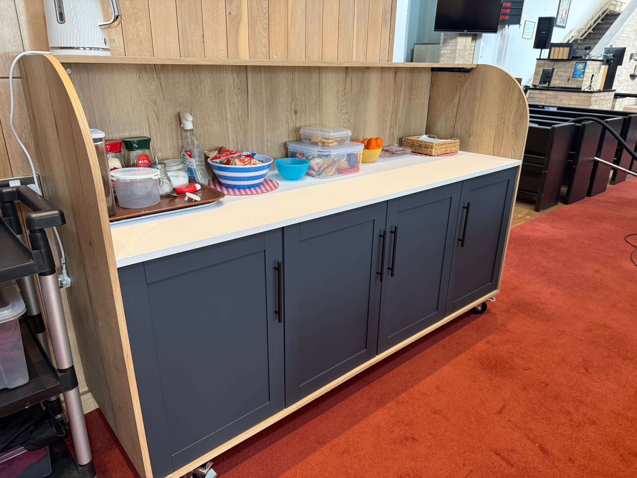 The new St Nick's refreshment and bar trolley: a wooden unit with dark grey cupboard doors and a white worktop, on castors in the church